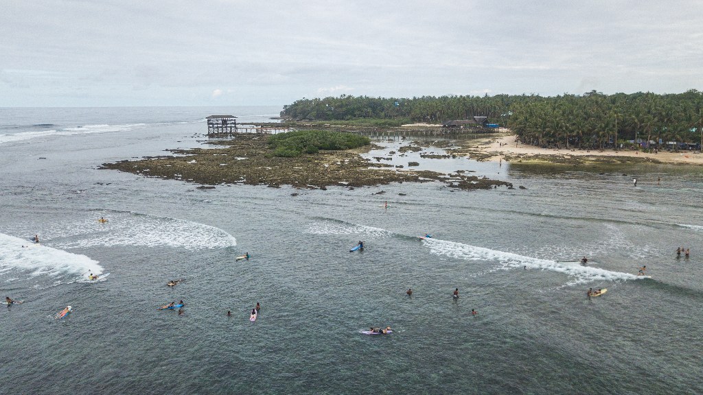Aerial of Cloud 9 beach surfing spot. Waves breaking over a reef in the Philippines, with beginner surfers in the water