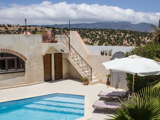 pool in the foreground of a beautiful white house with hills behind it in Taghazout Morocco